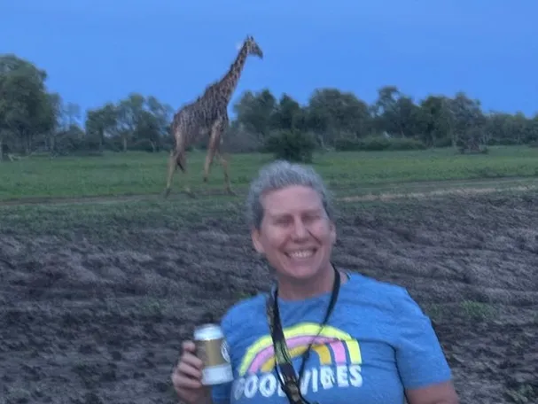 woman holding a beer with a giraffe walking